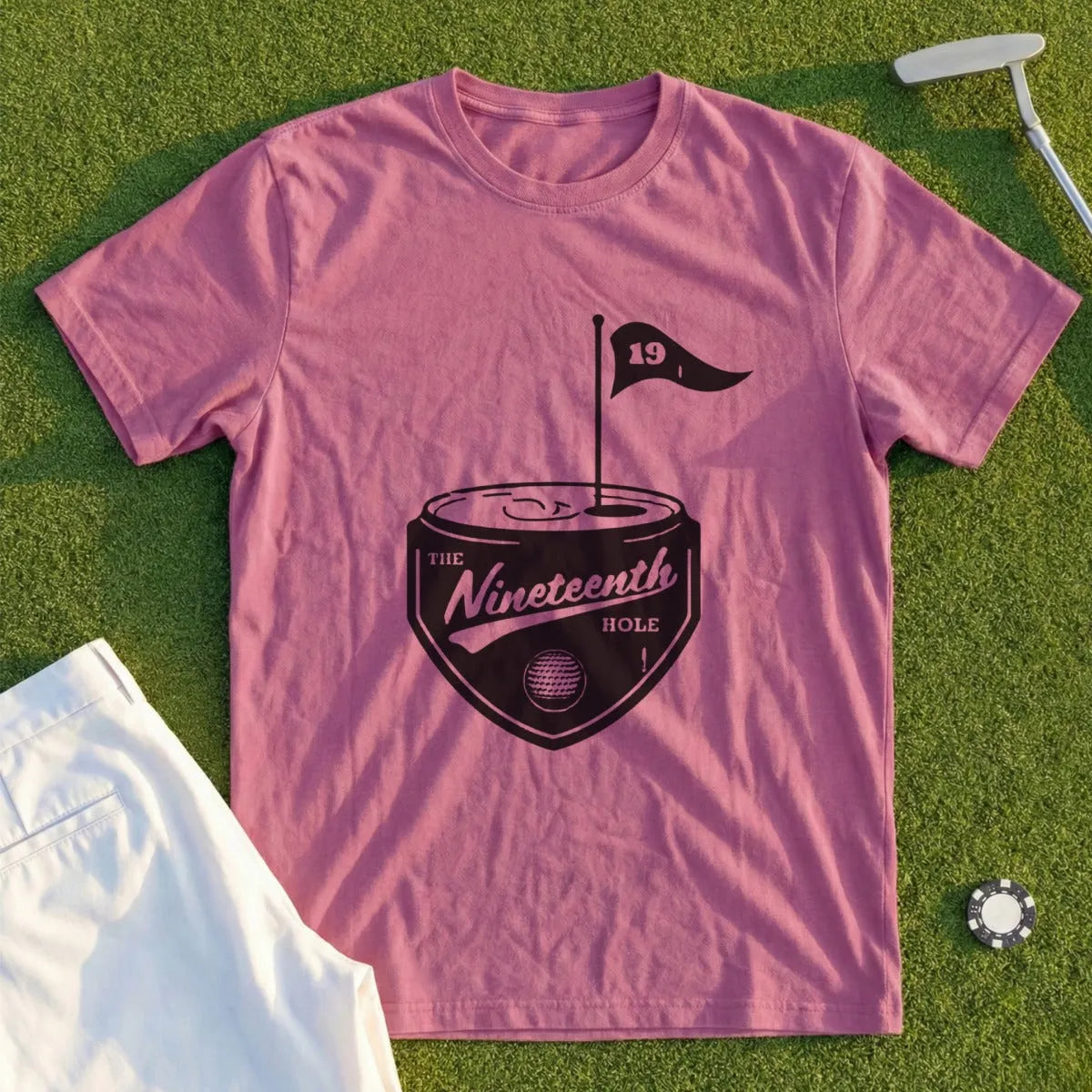 Pink t-shirt with a black golf-themed design and "The Nineteenth Hole" text.