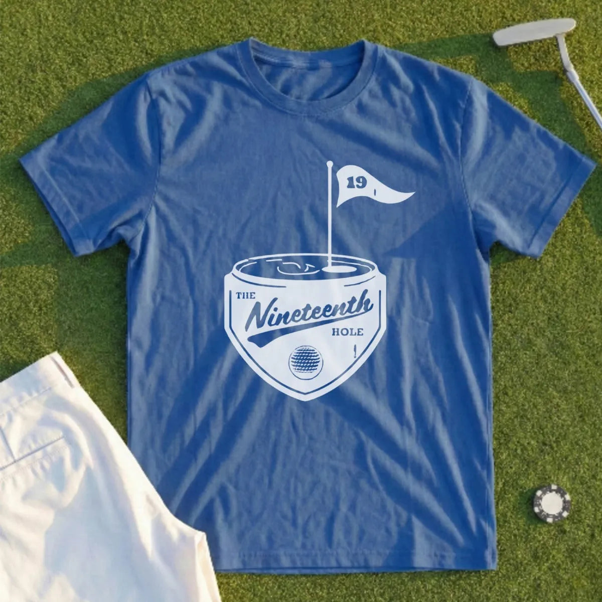 Blue t-shirt with "The Nineteenth Hole" golf-themed logo on a grass background.