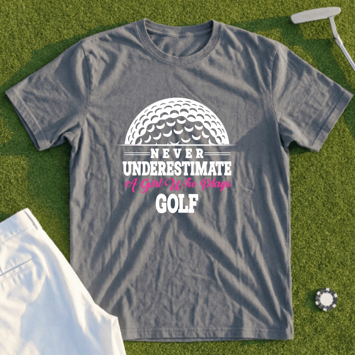 Grey t-shirt with "Never Underestimate A Girl Who Plays Golf" and golf ball graphic.