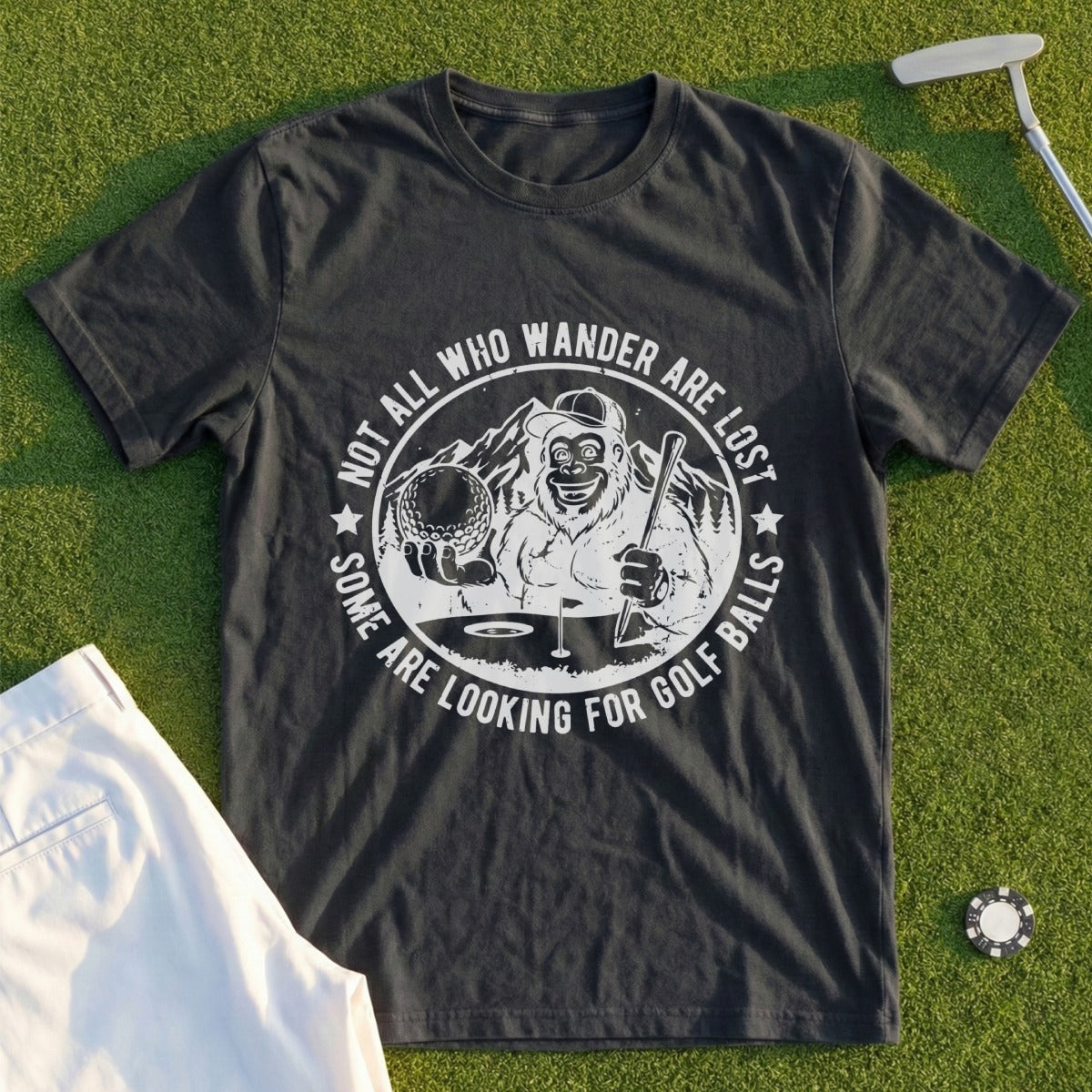 T-shirt with Bigfoot holding golf club and ball, text "NOT ALL WHO WANDER ARE LOST SOME ARE LOOKING FOR GOLF BALLS".