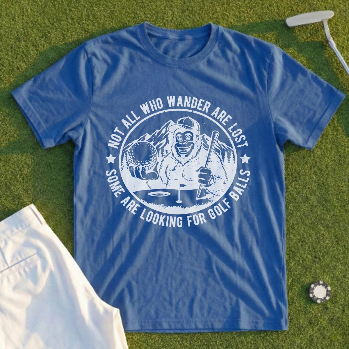 Blue t-shirt with Bigfoot holding a golf club and ball, text reads "Not all who wander are looking for golf balls".