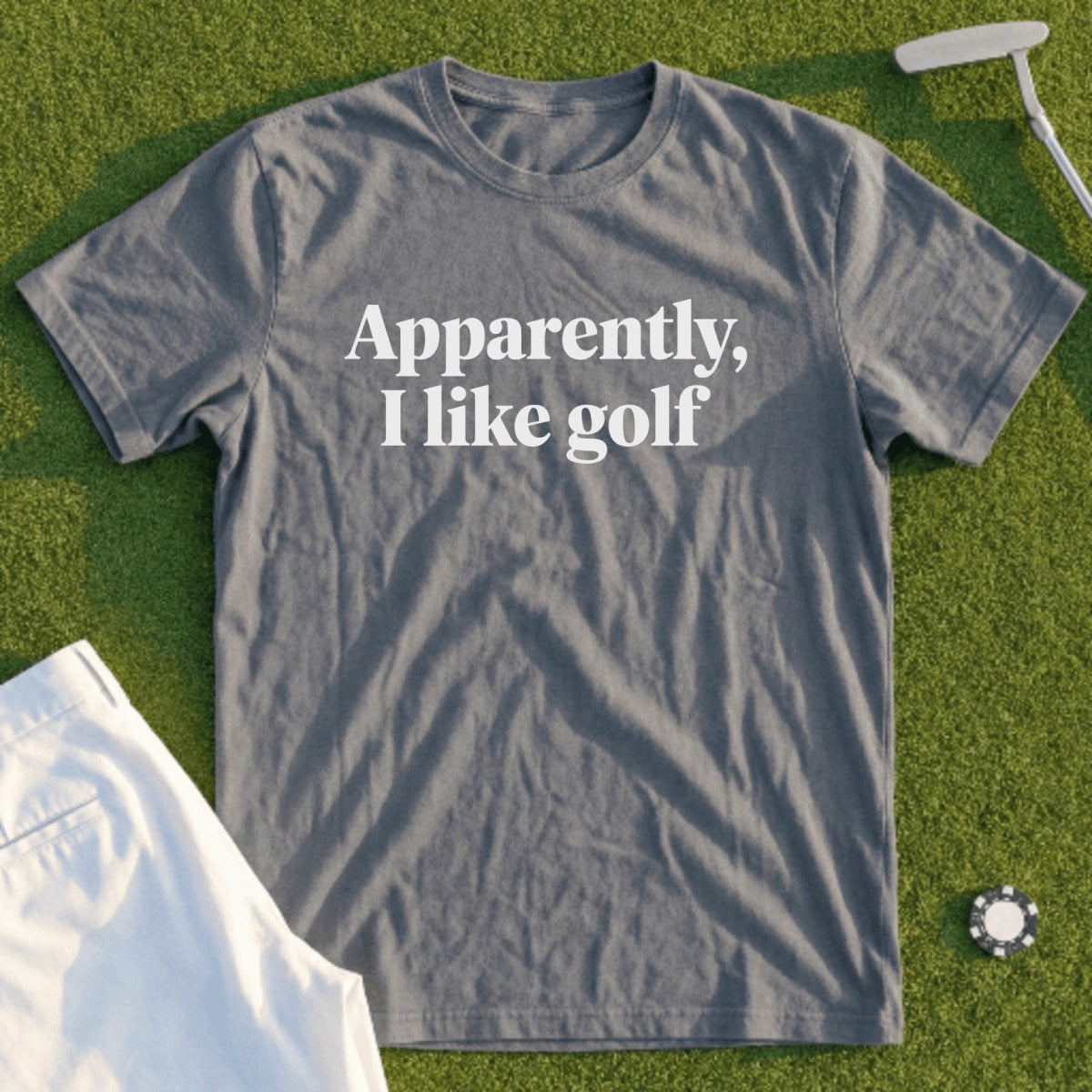 Gray t-shirt with "Apparently, I like golf" text, lying on grass.