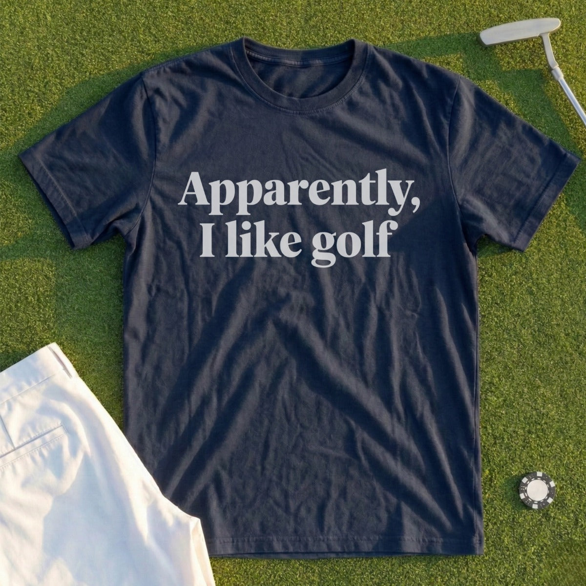 Navy t-shirt with white text "Apparently, I like golf" laid on grass.