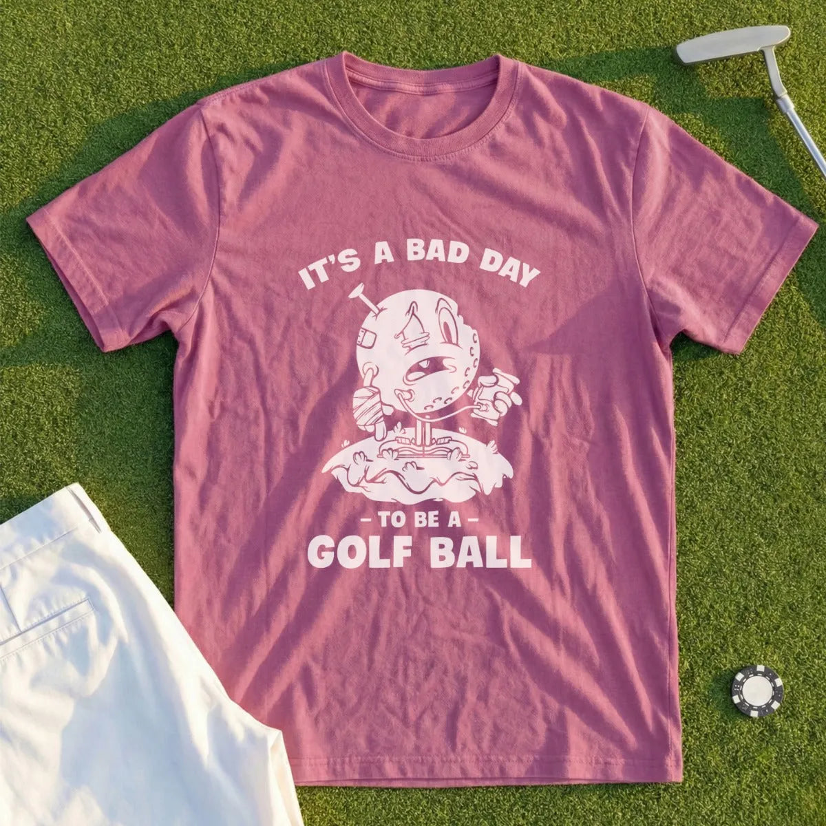 Pink t-shirt with cartoon golfer on a golf course, text "IT'S A BAD DAY TO BE A GOLF BALL".
