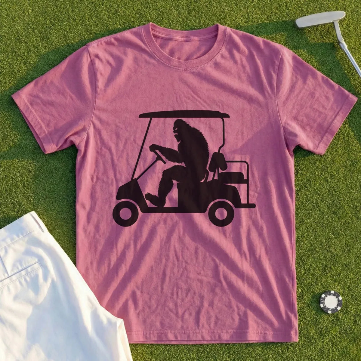 Bigfoot driving a golf cart on a dusty pink t-shirt.