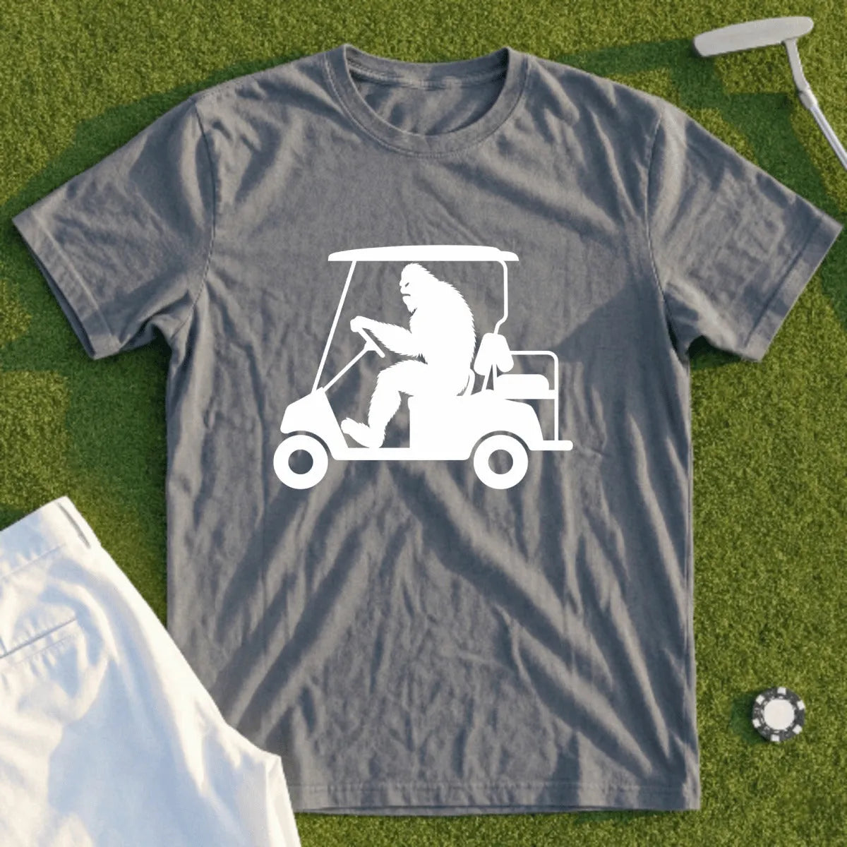 Silhouetted Bigfoot driving a golf cart on a grass background.