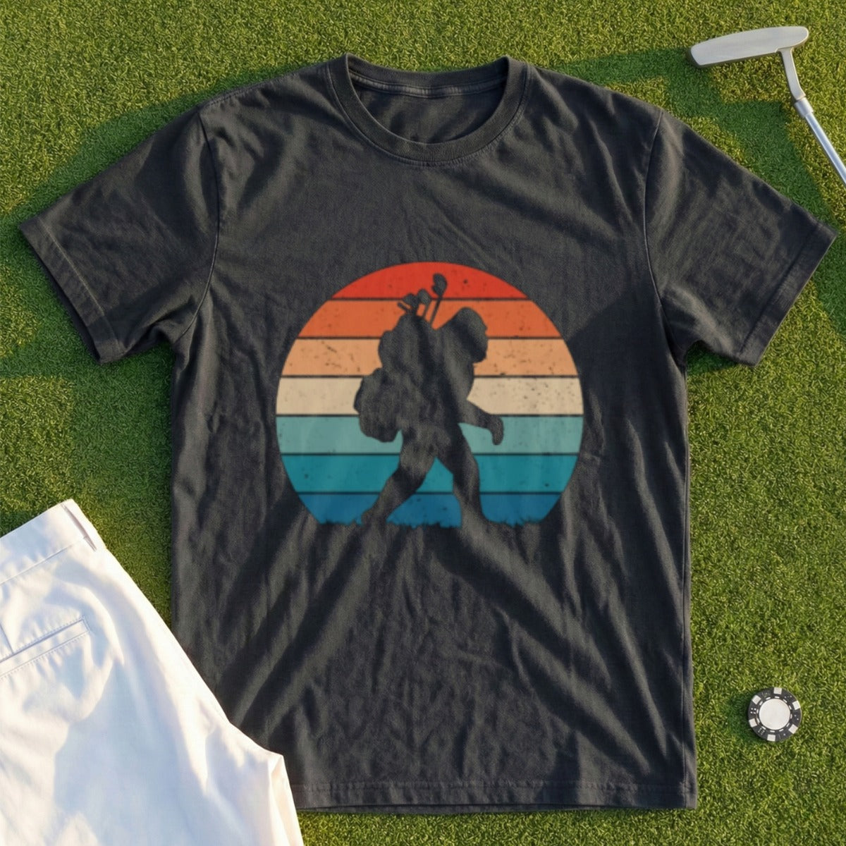Dark t-shirt with Bigfoot carrying golf bag against a retro sunset graphic.