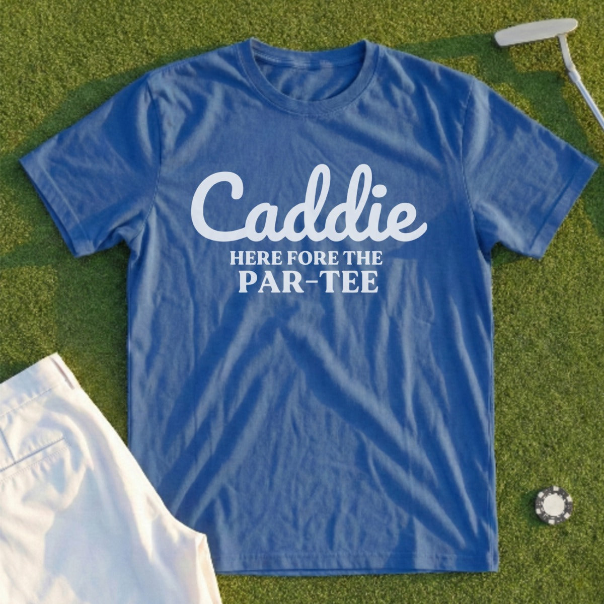 Blue t-shirt with "Caddie HERE FOR THE PAR-TEE" text, on grass with golf items.