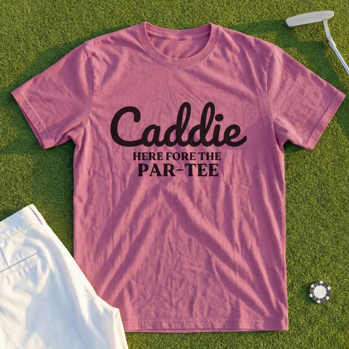 Pink t-shirt with black text "Caddie HERE FORE THE PAR-TEE" on a golf course.