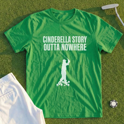 Green t-shirt with white text and golfer graphic, lying on grass.