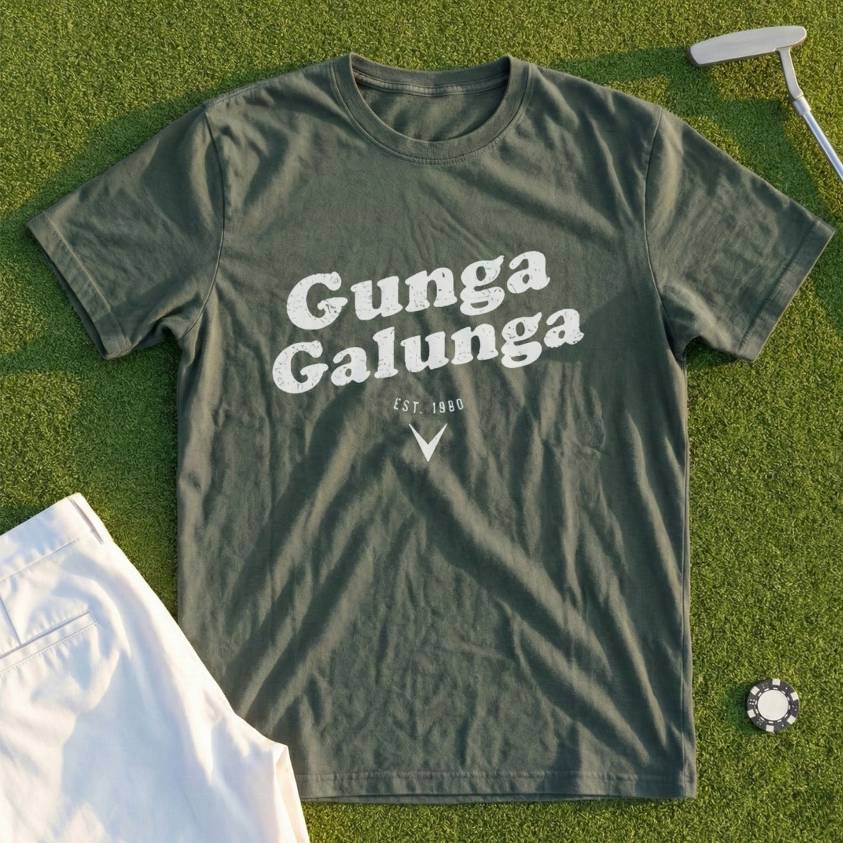 Green t-shirt with "Gunga Galunga est. 1980" text, on grass with golf accessories.