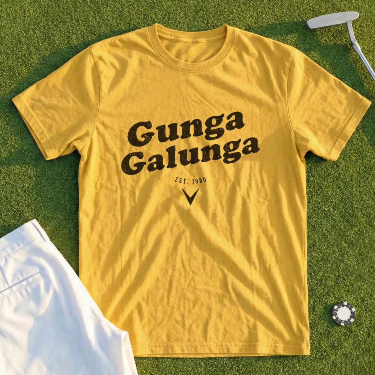 Yellow t-shirt with "Gunga Galunga" text, golf tee, and tee on grass.