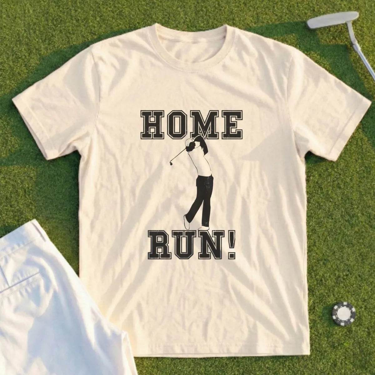 Cream t-shirt with "HOME RUN!" text and golfer graphic on grass.