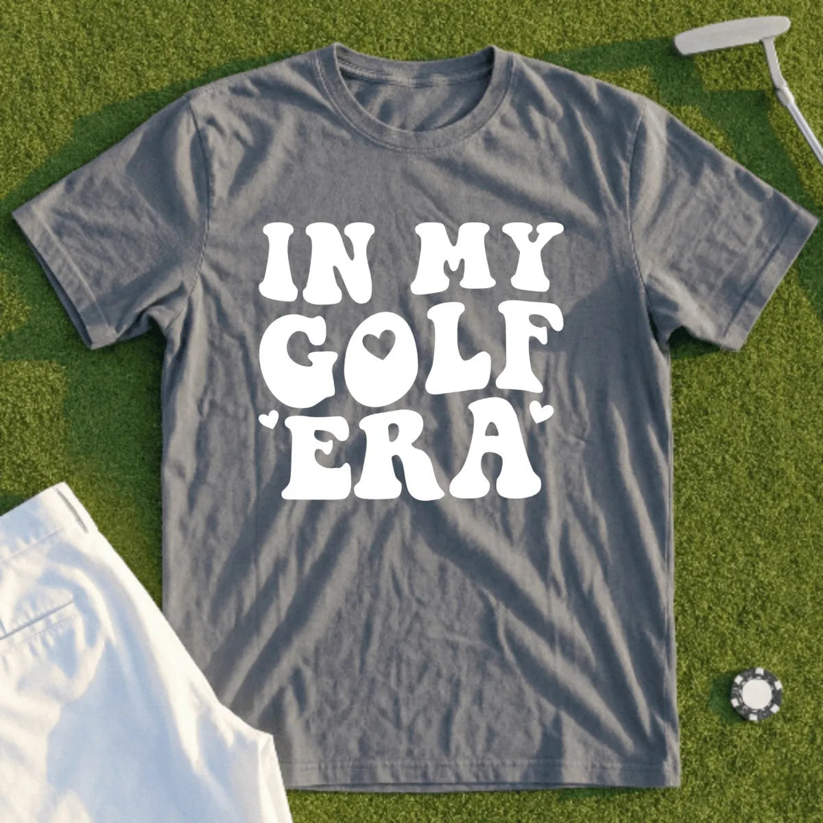Gray t-shirt with "IN MY GOLF ERA" text in white, laid on grass.
