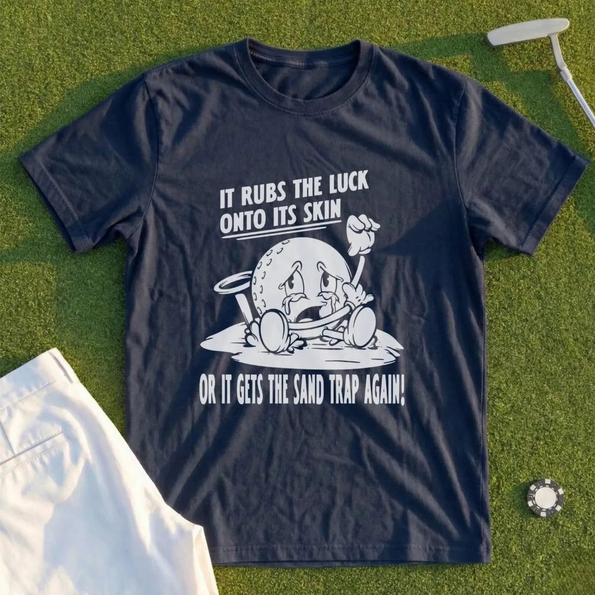 Navy t-shirt with cartoon golf ball lamenting "It rubs the luck onto its skin or it gets the sand trap again!"