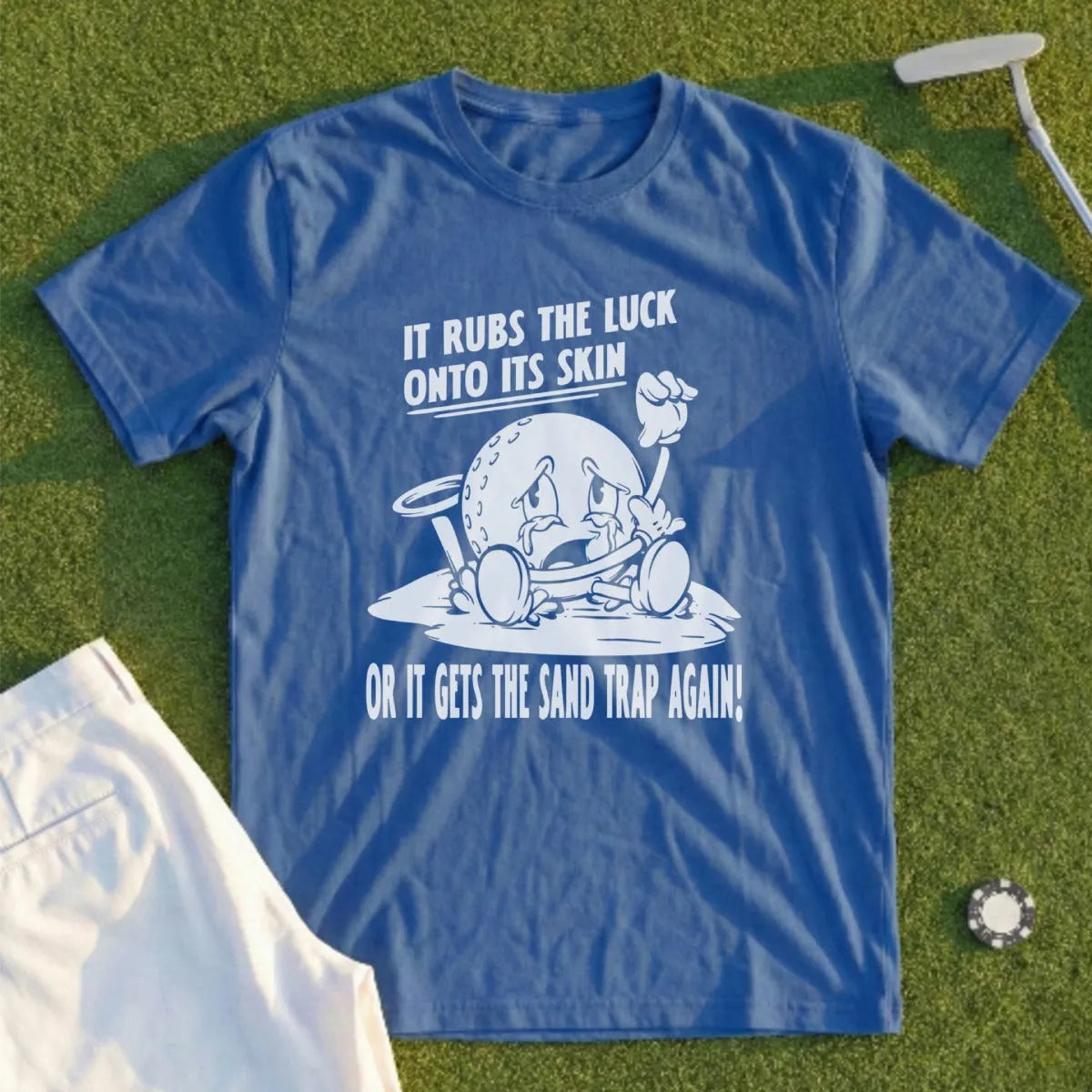 Blue t-shirt with cartoon golf ball text: "It rubs the luck onto its skin or it gets the sand trap again!"