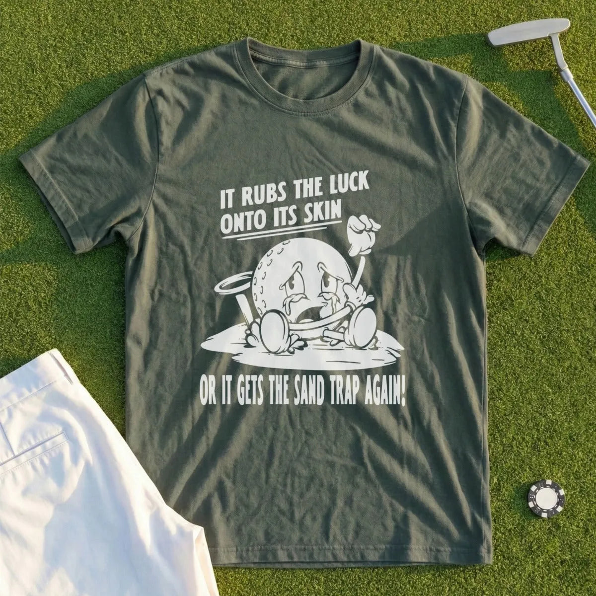 Green t-shirt with cartoon golf ball saying "It rubs the luck onto its skin or it gets the sand trap again!".