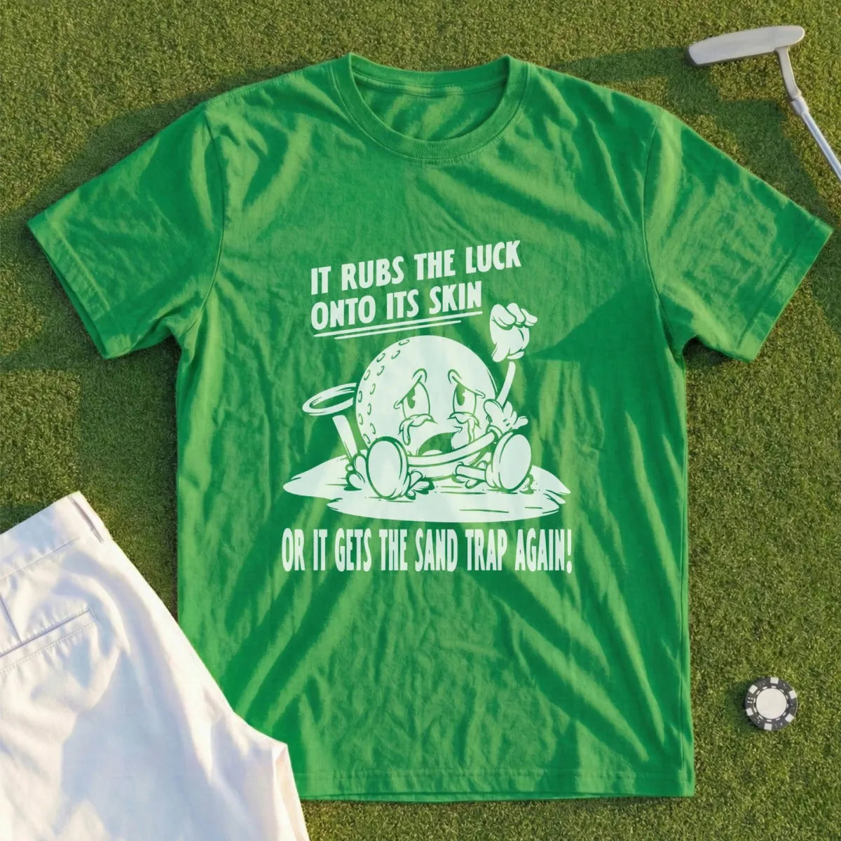 Green t-shirt with golf ball cartoon saying "It rubs the luck onto its skin or it gets the sand trap again!"