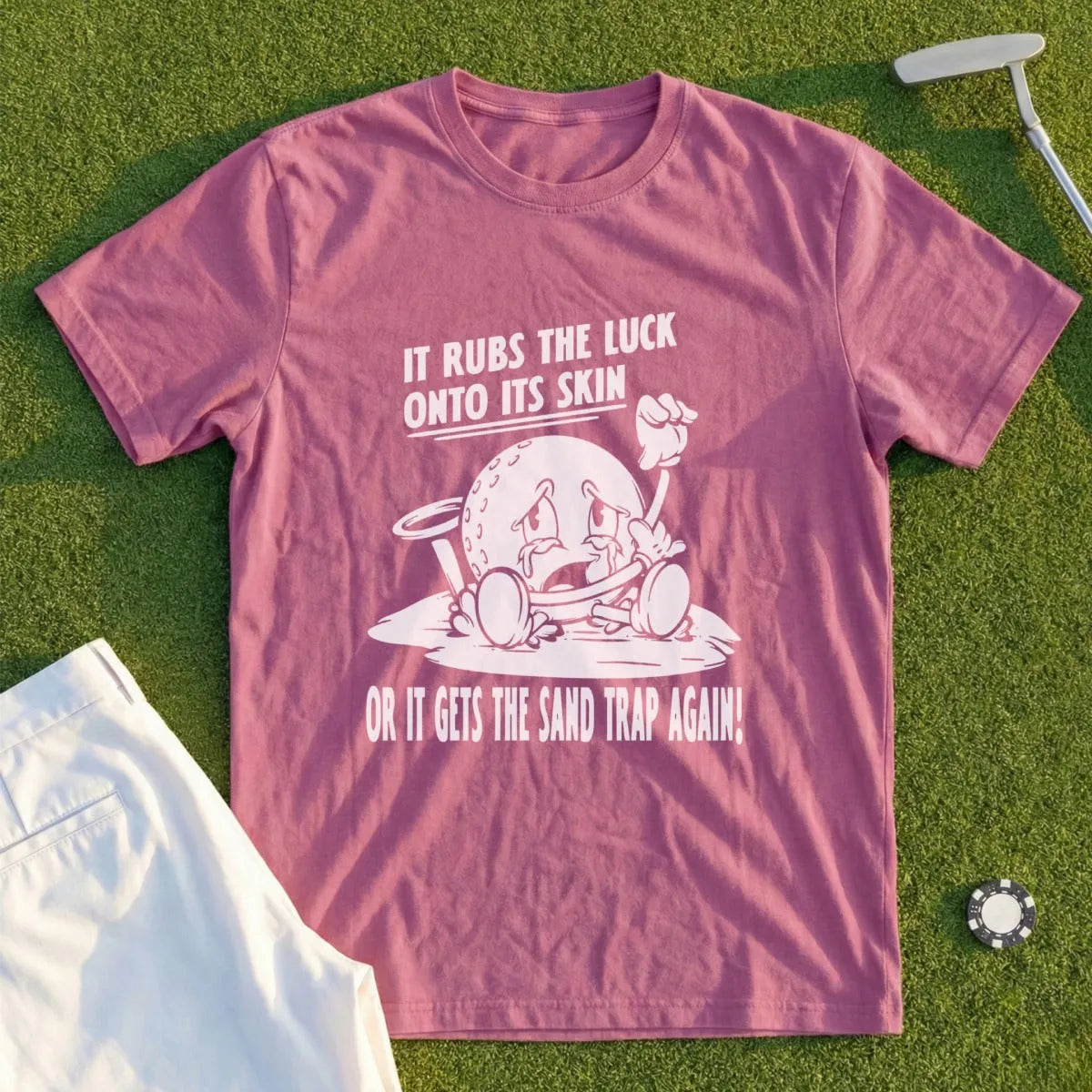 Pink t-shirt with cartoon golf ball saying "It rubs the luck onto its skin or it gets the sand trap again!".