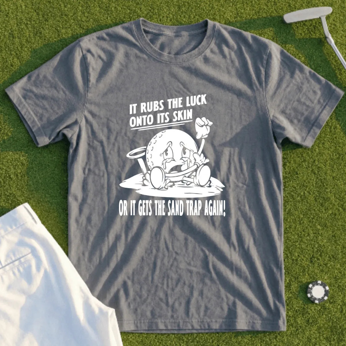 Grey t-shirt with cartoon golf ball and text "It rubs the luck onto its skin or it gets the sand trap again!".
