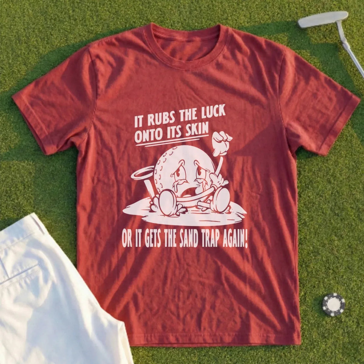 Maroon t-shirt with cartoon golf ball crying "It rubs the luck onto its skin or it gets the sand trap again!"