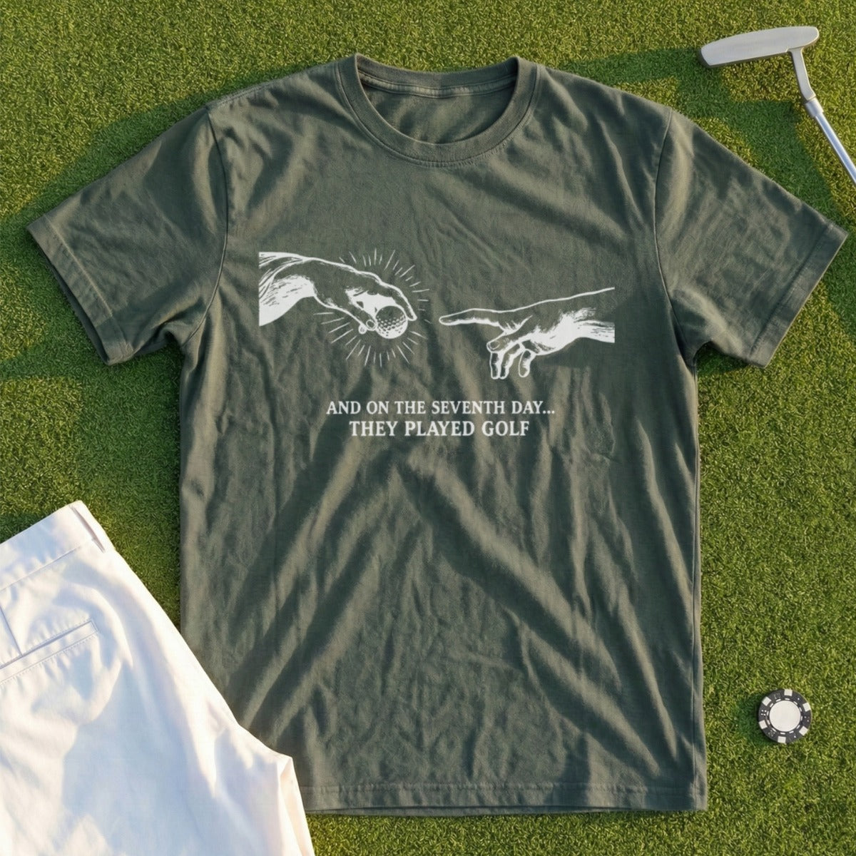 Olive green t-shirt with "The Creation of Adam" hands and text "AND ON THE SEVENTH DAY... THEY PLAYED GOLF".