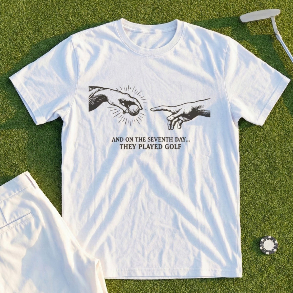 White t-shirt with a graphic of two hands reaching for a golf ball and text.