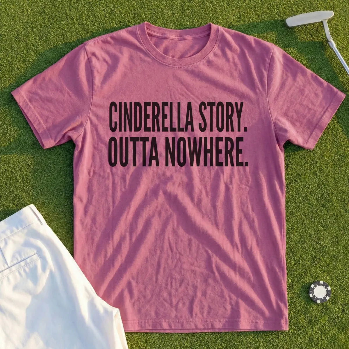 Pink t-shirt with "Cinderella Story. Outta Nowhere." text, lying on grass.