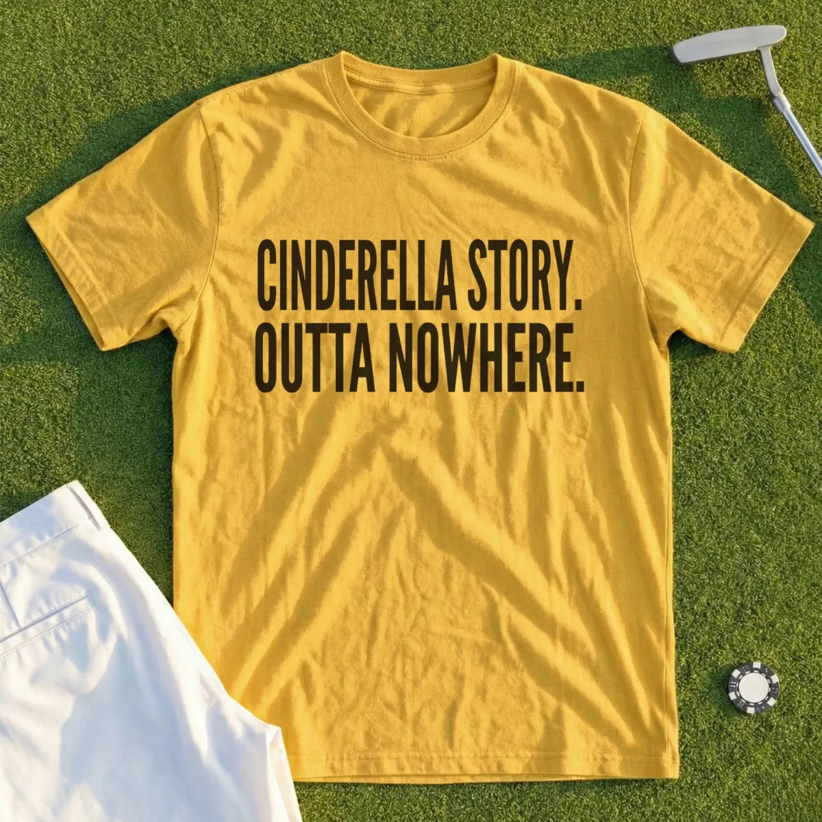 Yellow t-shirt with "Cinderella Story. Outta Nowhere." text, folded white pants, golf club.