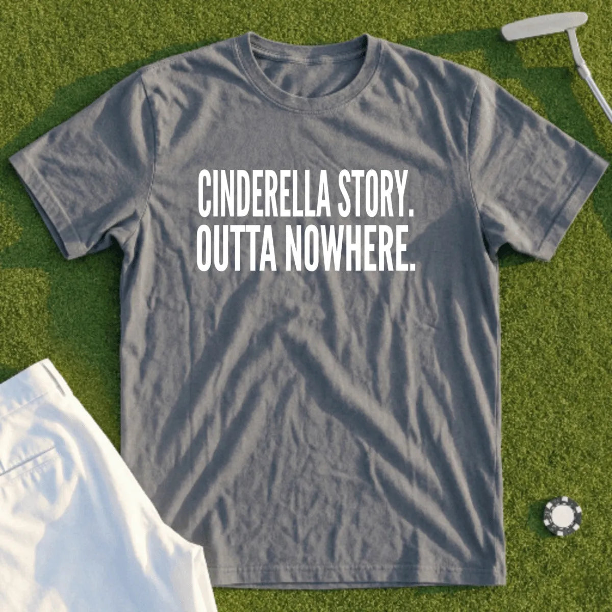 Grey t-shirt with "Cinderella Story. Outta Nowhere." text, laid on grass.