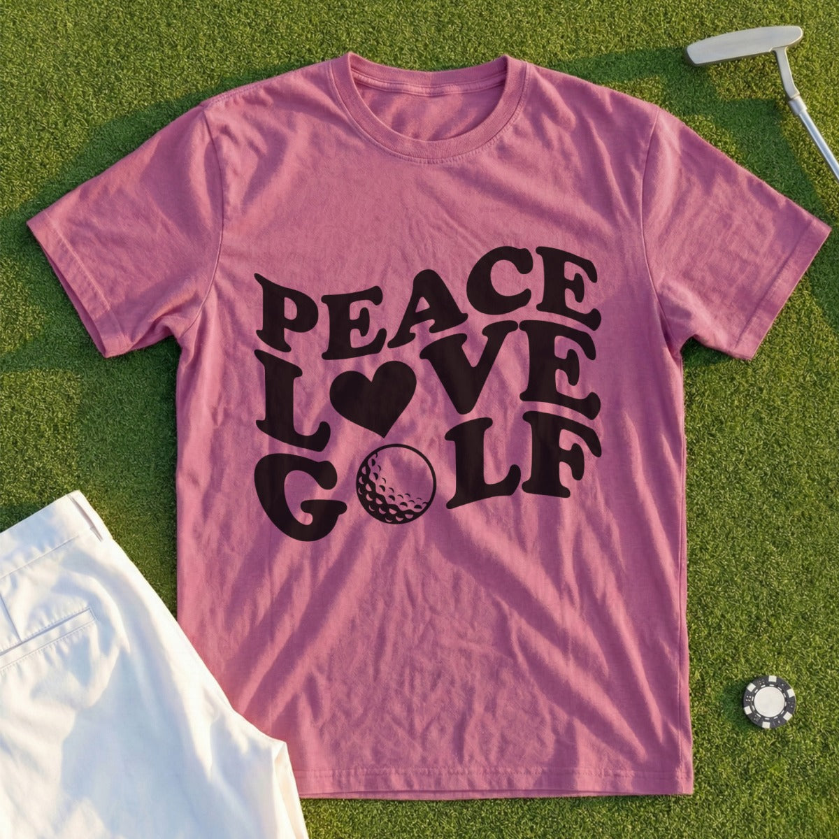 Pink t-shirt with "Peace Love Golf" text and golf ball graphic on grass.
