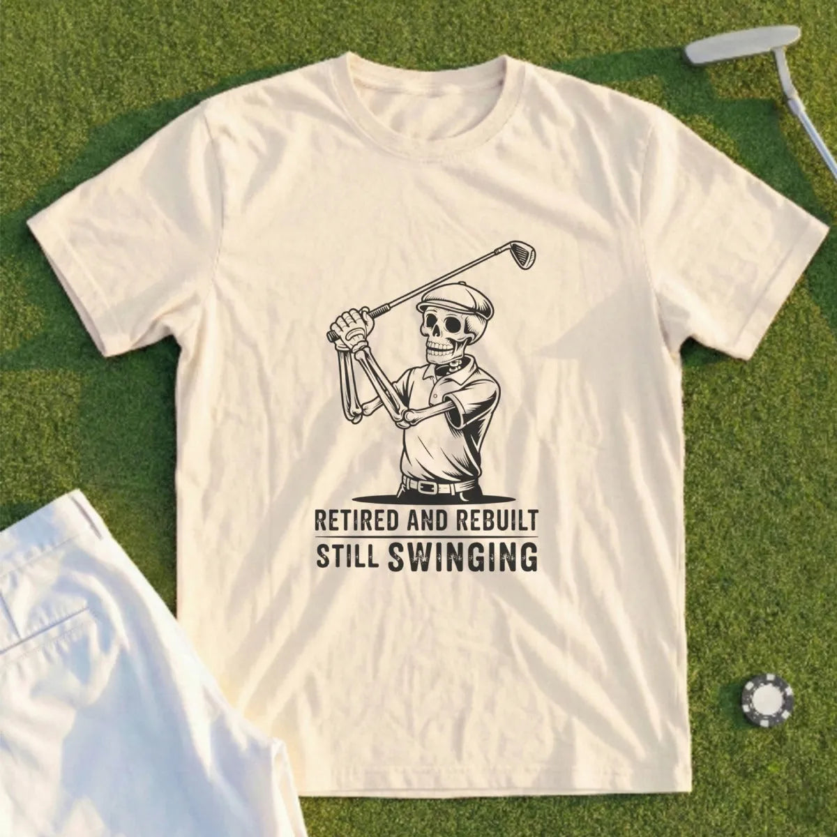 Cream t-shirt with skeleton golfer graphic and text "Retired and Rebuilt Still Swinging".