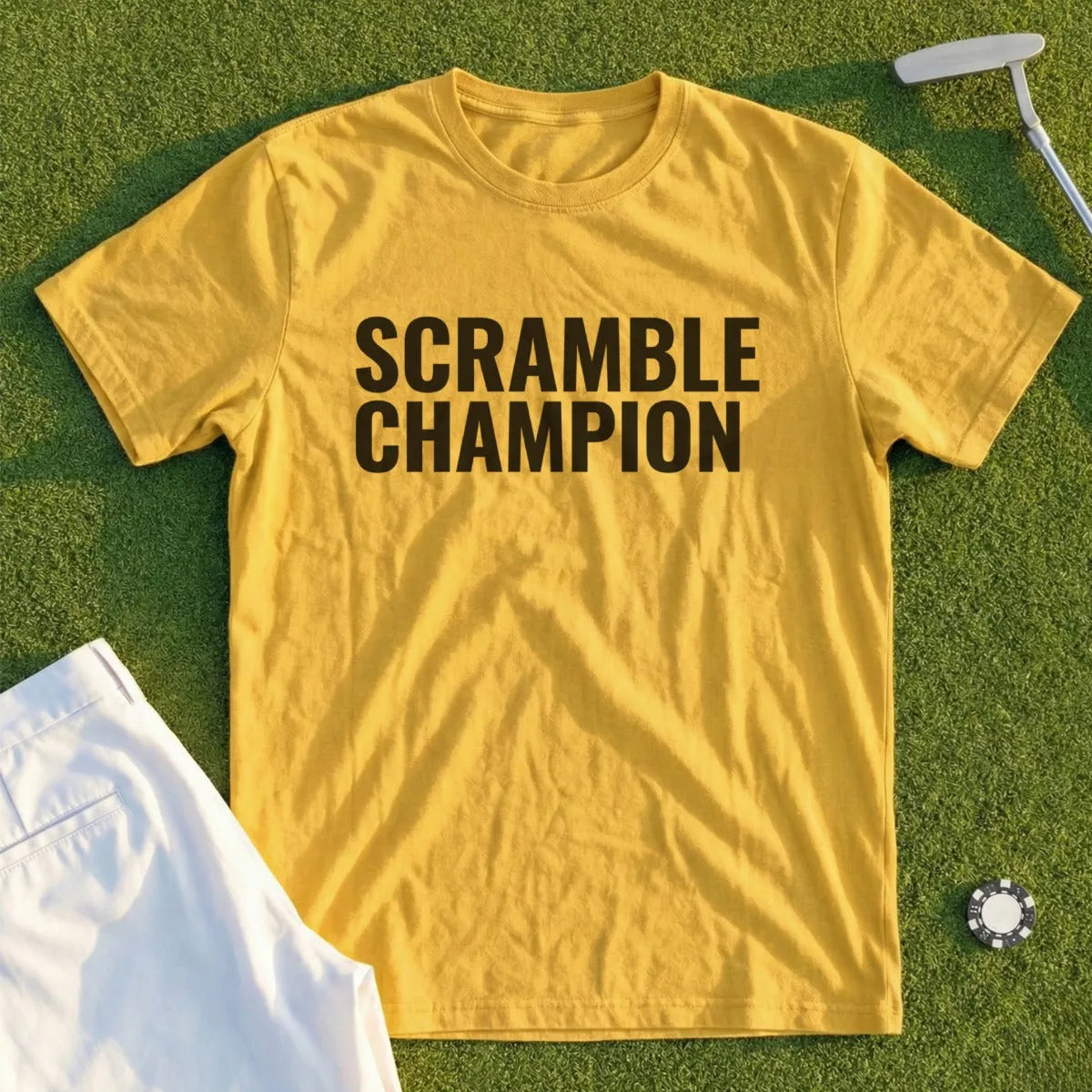 Yellow t-shirt with "SCRAMBLE CHAMPION" text, laid flat on grass with golf attire.