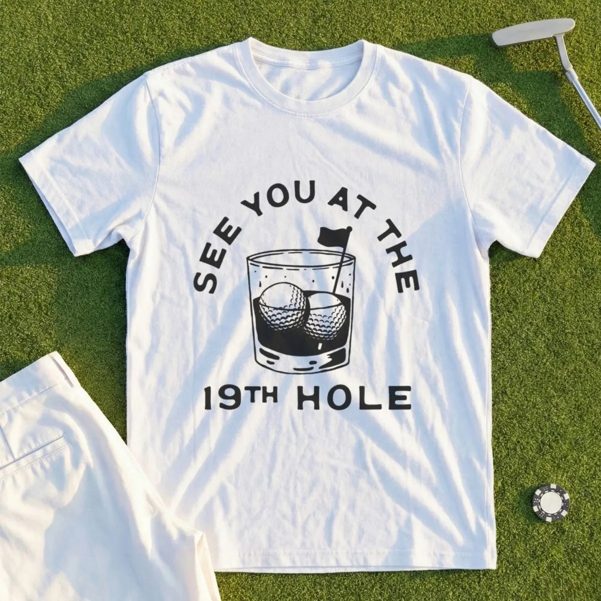 White t-shirt with "See You At The 19th Hole" and golf balls in a glass.