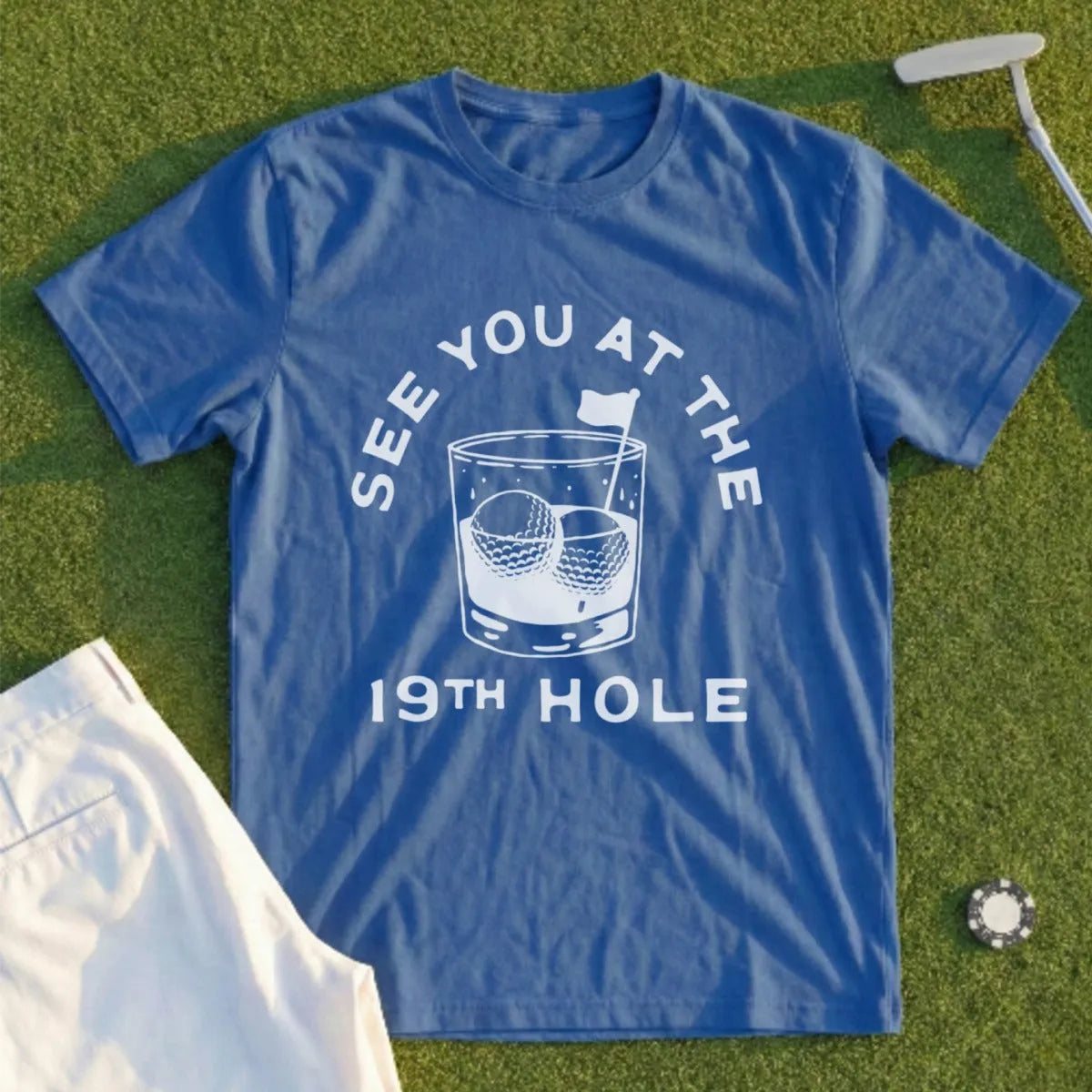 Blue t-shirt with text "SEE YOU AT THE 19TH HOLE" above golf balls in a glass.