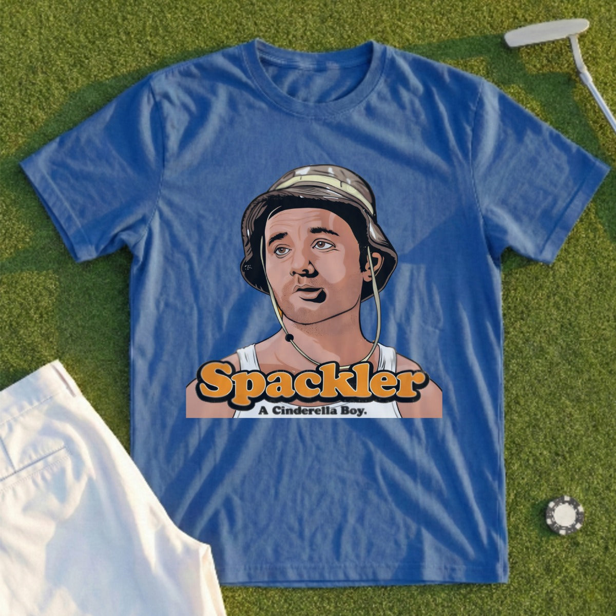Blue t-shirt with cartoon character "Spackler A Cinderella Boy" and a golf course background.