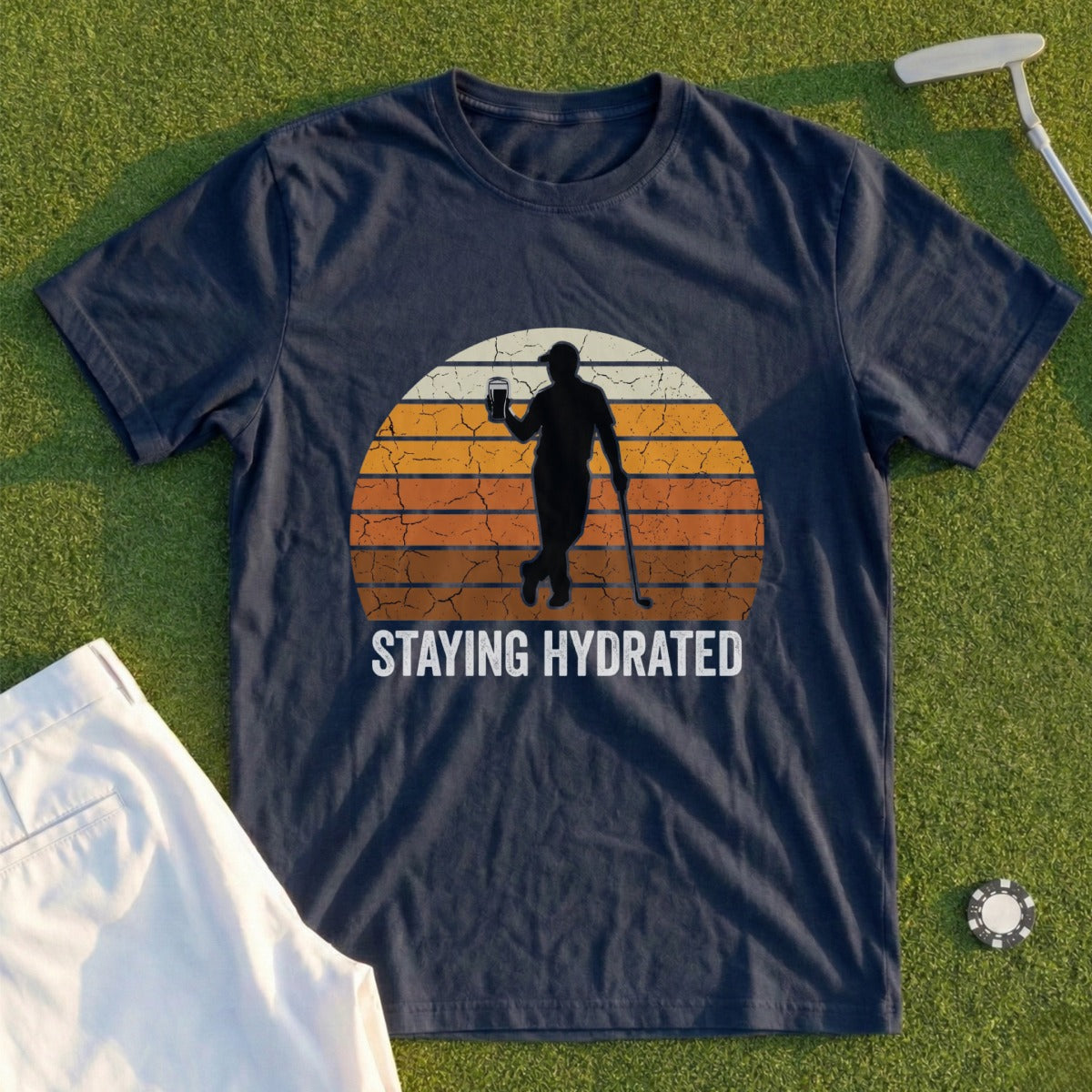Navy t-shirt with a golfer silhouette holding a drink at sunset, text "STAYING HYDRATED".