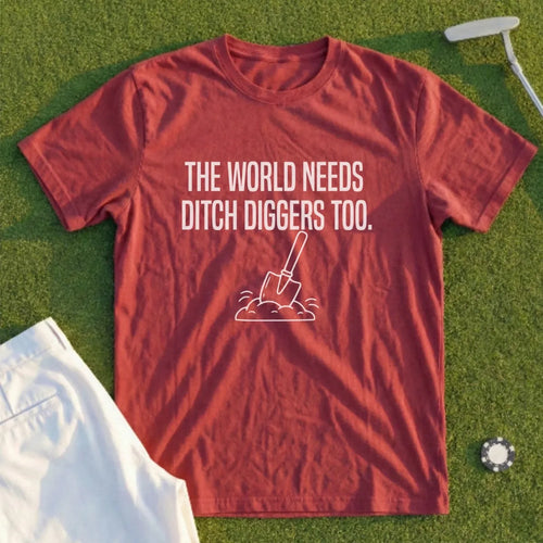 Maroon t-shirt with white text and shovel graphic on grass background.