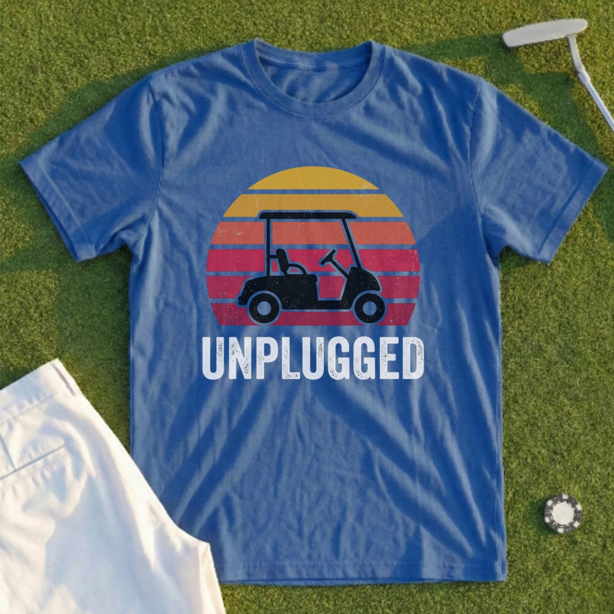 Blue t-shirt with golf cart graphic and "UNPLUGGED" text on a sunset background.