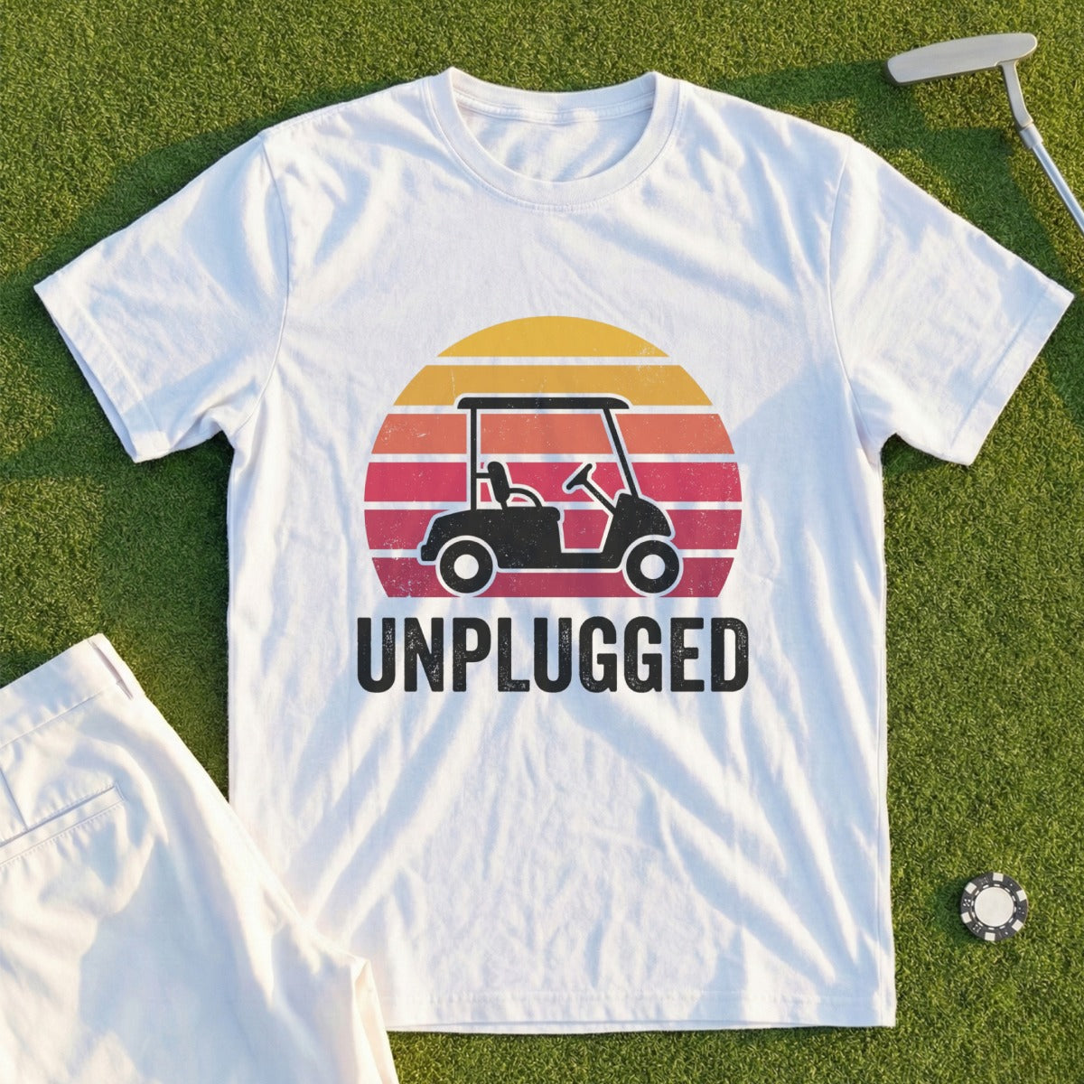 White t-shirt with "UNPLUGGED" text and golf cart graphic on sunset background.