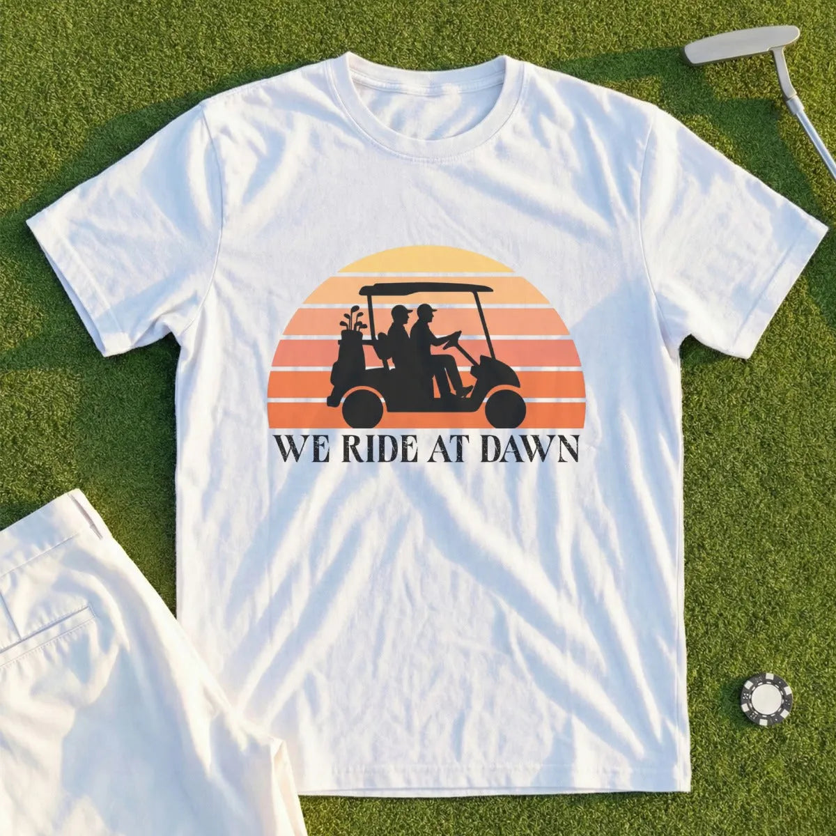 White t-shirt with "We Ride at Dawn" and golf cart sunset graphic.