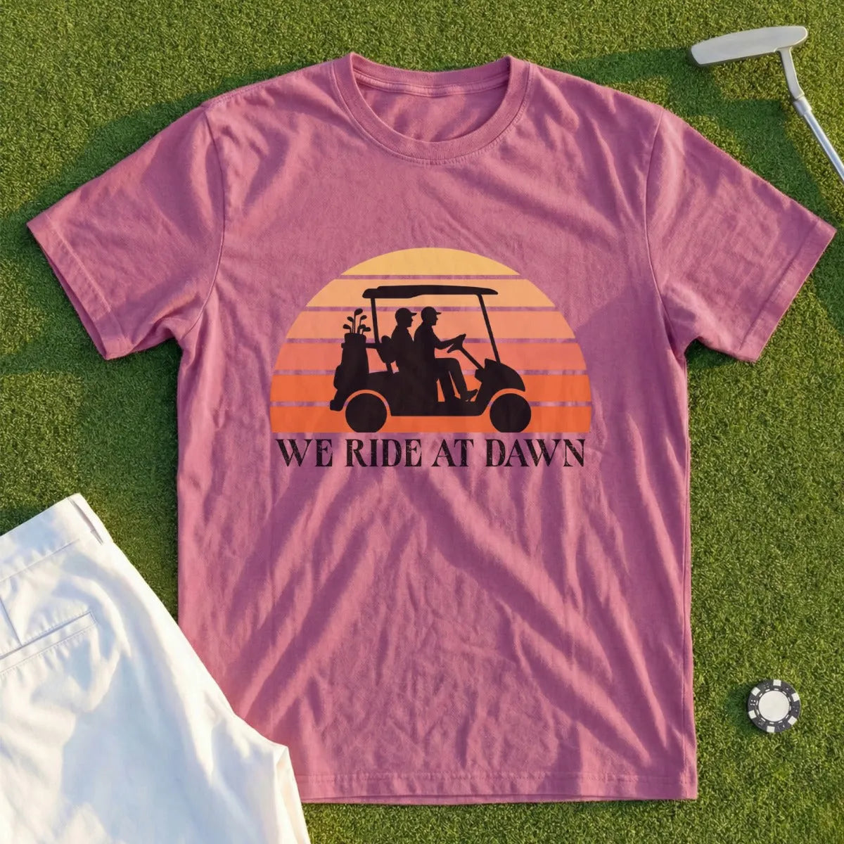 Pink t-shirt with "WE RIDE AT DAWN" text and golf cart silhouette.