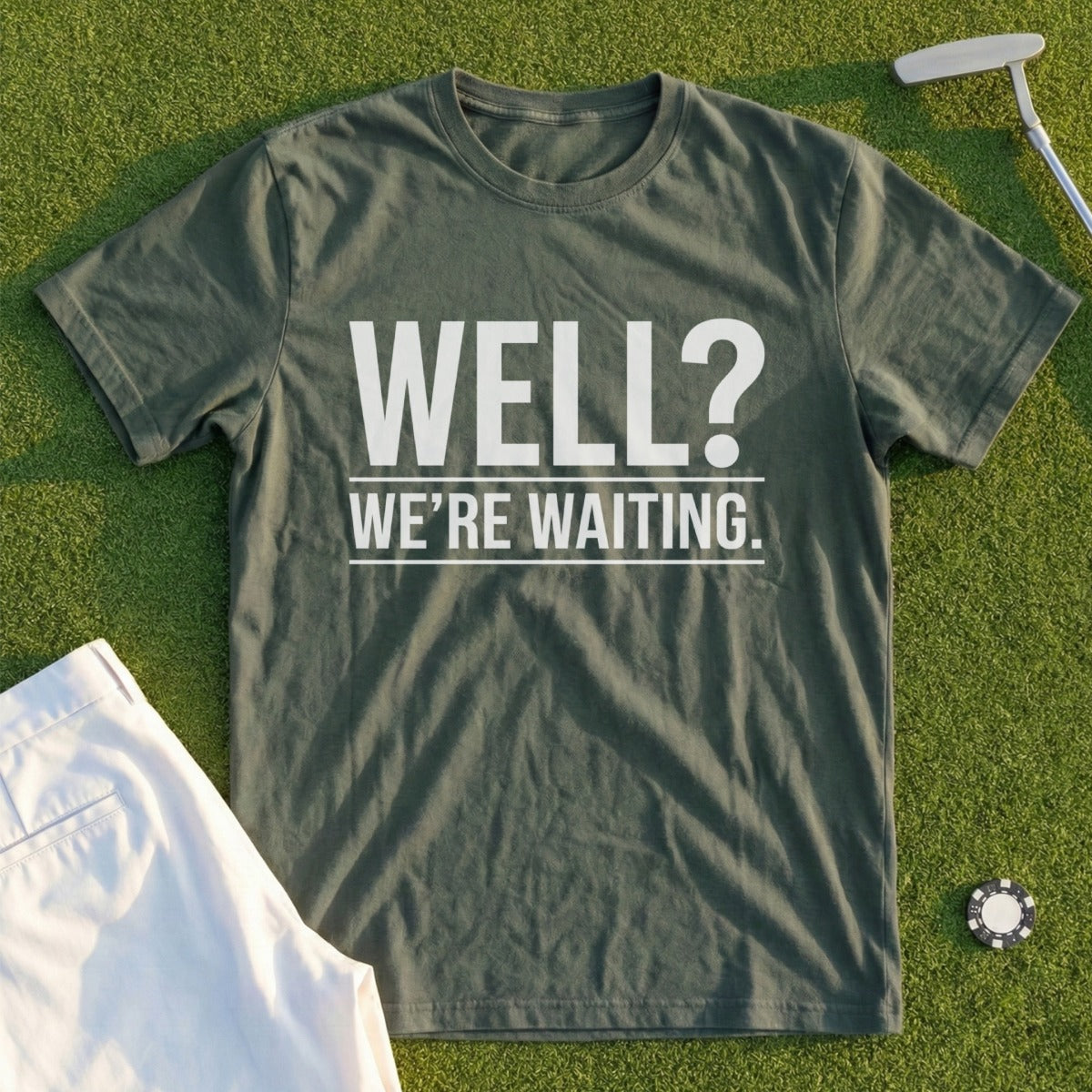 Green t-shirt with white text "WELL? WE'RE WAITING." on a grass background.