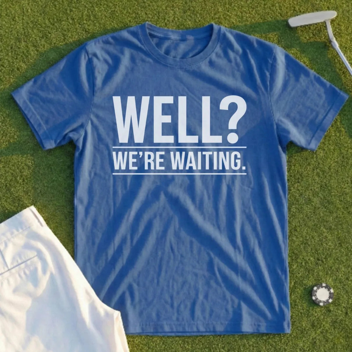 Blue t-shirt with white text "WELL? WE'RE WAITING." on a golf course.