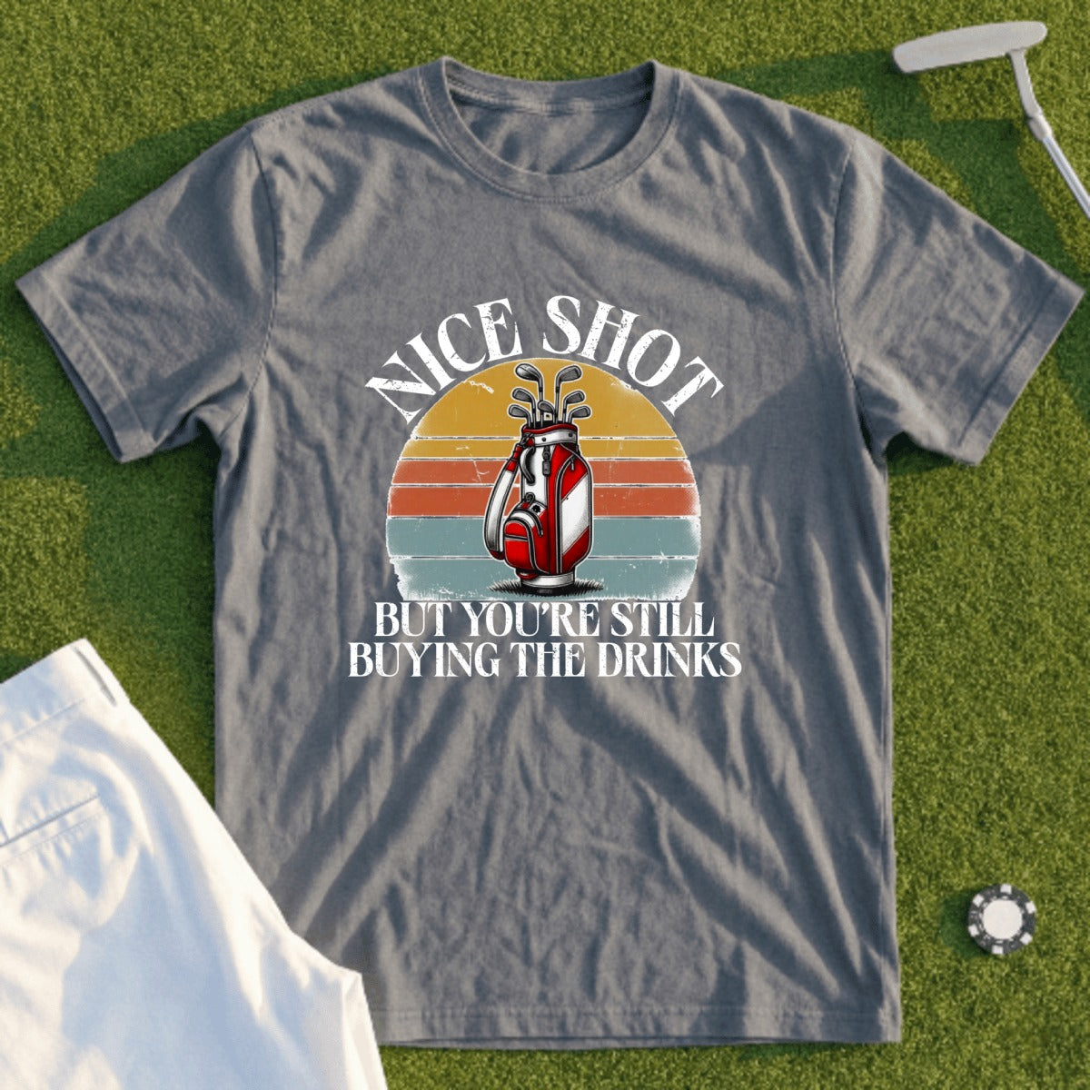 Grey t-shirt with a vintage sunset graphic and golf bag, featuring text "Nice Shot But You're Still Buying The Drinks".