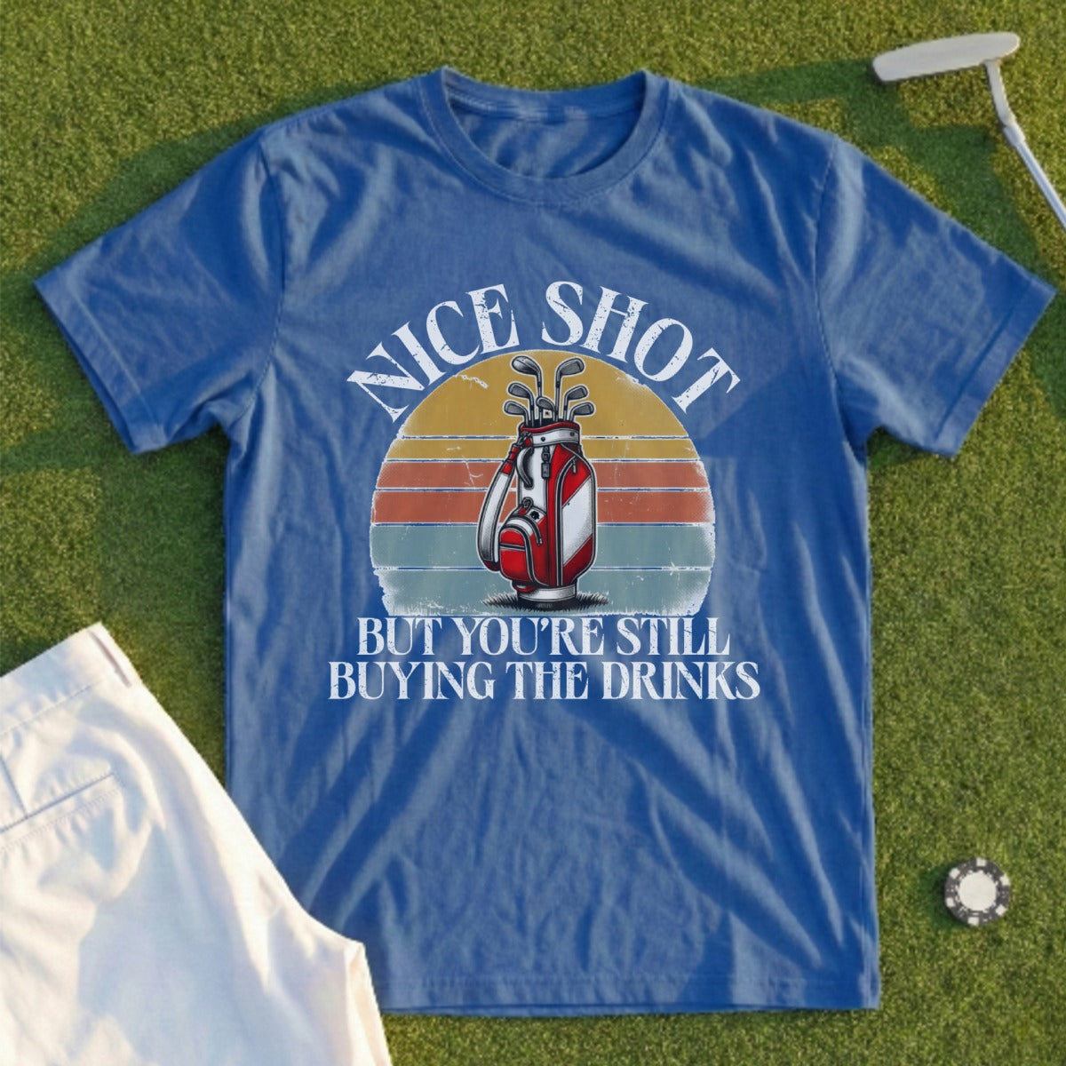 Blue t-shirt with "Nice shot but you're still buying the drinks" text and golf bag graphic.