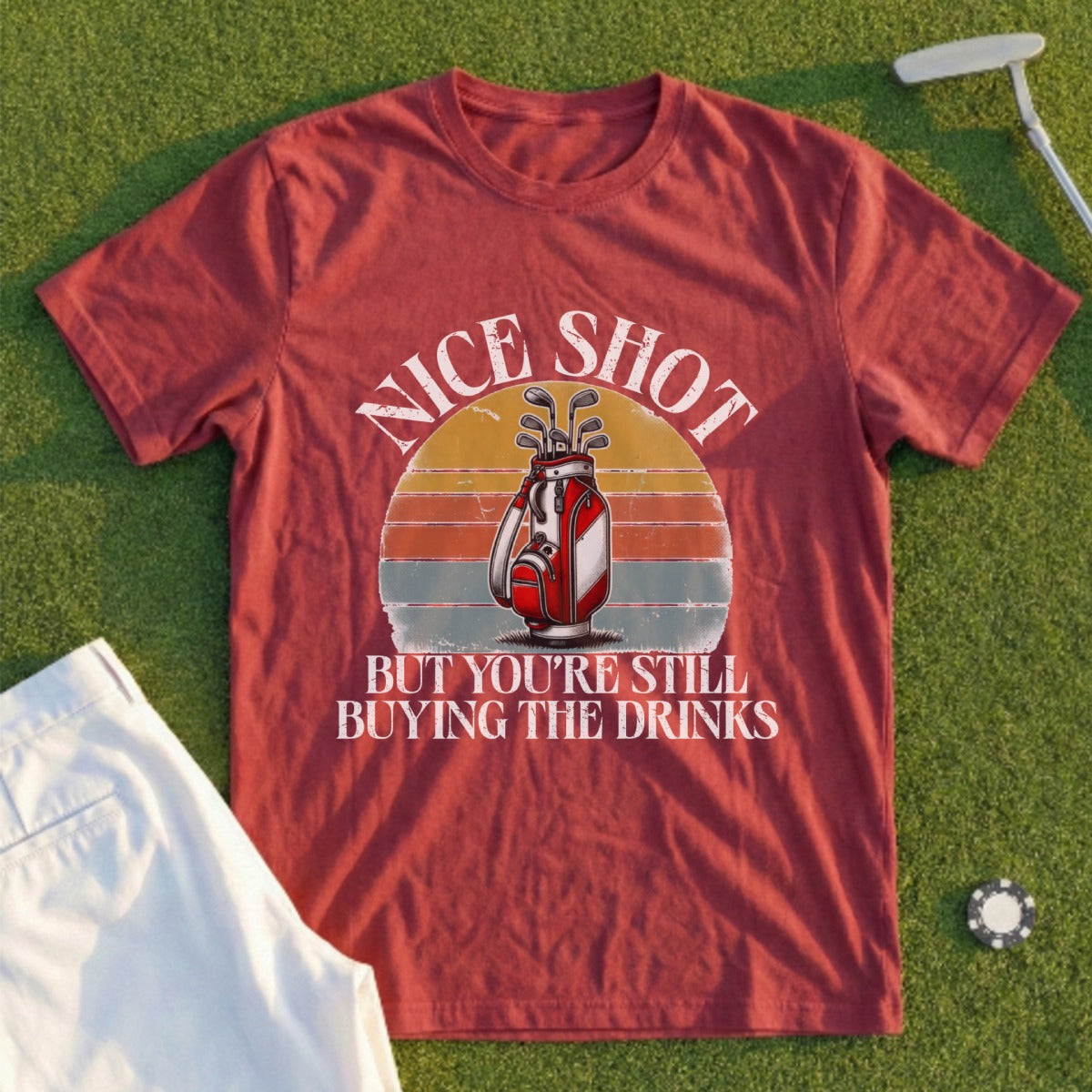 Maroon t-shirt with a graphic of a golf bag and the text "NICE SHOT BUT YOU'RE STILL BUYING THE DRINKS".
